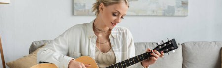 Photo for Cheerful blonde woman playing acoustic guitar in living room, banner - Royalty Free Image