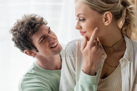 cheerful man in sweatshirt touching face of pretty and blonde girlfriend 