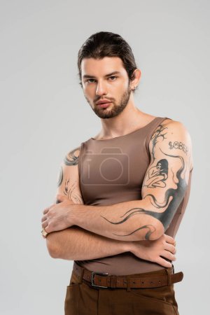 Portrait of young tattooed man looking at camera isolated on grey 