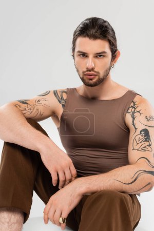 Foto de Stylish tattooed man in sleeveless short sitting on grey background - Imagen libre de derechos