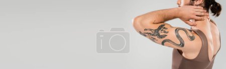 Cropped view of muscular man in tank top touching neck isolated on grey, banner 