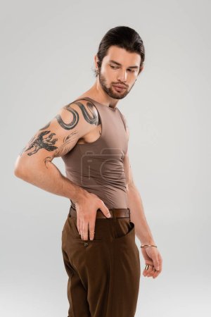 Brunette bearded man with tattoo posing isolated on grey  Poster 637403140