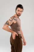 Brunette bearded man with tattoo posing isolated on grey  Poster #637403140