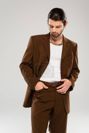 Trendy young man posing in brown suit isolated on grey 