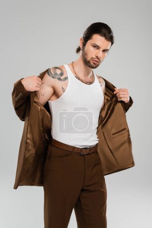 Stylish tattooed man in tank top wearing jacket isolated on grey 