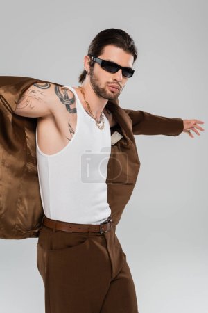 Fashionable tattooed man posing in jacket isolated on grey 