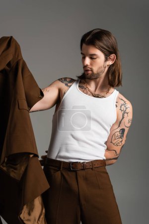 Long haired man with tattoo wearing jacket isolated on grey 