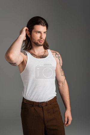 Photo for Stylish long haired man in tank top touching hair isolated on grey - Royalty Free Image