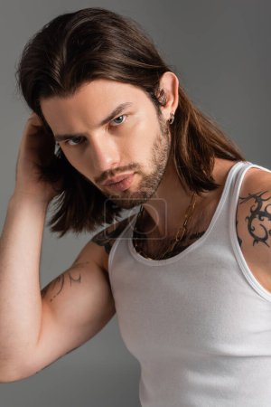 Portrait of long haired man with tattoo touching hair isolated on grey 