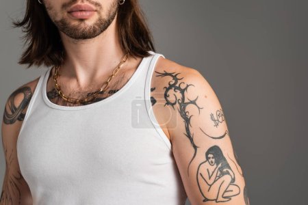Cropped view of brunette tattooed model standing isolated on grey 