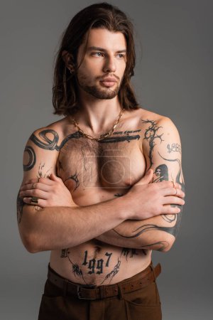 Muscular and tattooed model crossing arms isolated on grey 