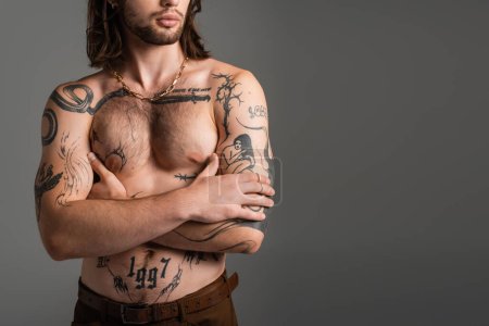 Cropped view of long haired and tattooed man crossing arms isolated on grey 