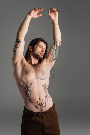 Foto de Sexy tattooed man posing and closing eyes isolated on grey - Imagen libre de derechos