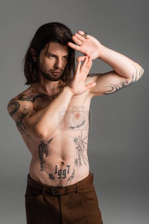 Photo for Bearded long haired model with tattoo on torso posing isolated on grey - Royalty Free Image