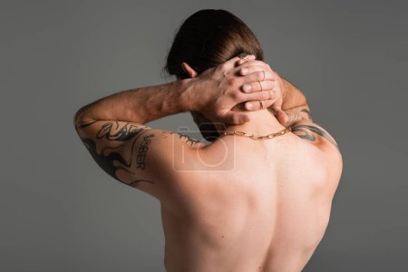 Back view of shirtless tattooed man touching neck isolated on grey 