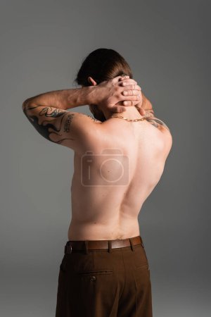 Shirtless and tattooed model touching neck isolated on grey 