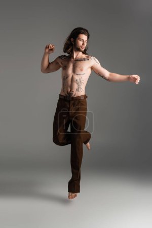 Foto de Shirtless and tattooed man jumping on grey background - Imagen libre de derechos