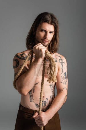 Photo for Shirtless tattooed man holding rope and looking at camera isolated on grey - Royalty Free Image