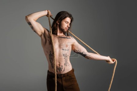 Photo for Muscular and tattooed man holding rope isolated on grey - Royalty Free Image