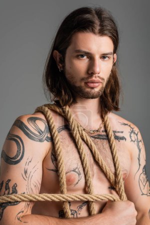 Portrait of sexy tattooed man holding rope isolated on grey 
