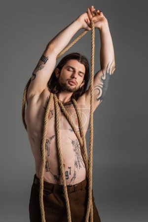 Photo for Muscular tattooed model posing with rope isolated on grey - Royalty Free Image