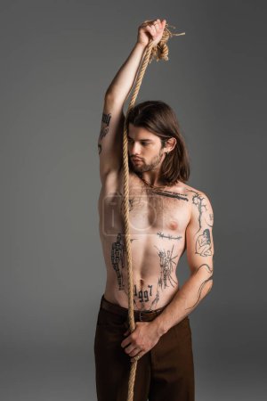 Photo for Shirtless tattooed man holding rope and looking away isolated on grey - Royalty Free Image