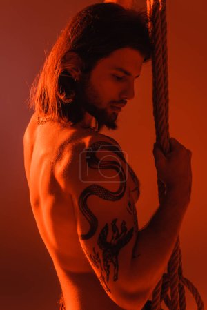 Foto de Sexy tattooed model holding rope isolated on red - Imagen libre de derechos