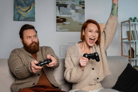 Photo for KYIV, UKRAINE - DECEMBER 16, 2022: Excited woman holding joystick near husband at home - Royalty Free Image