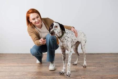 Lächelnde rothaarige Frau umarmt Dalmatiner-Hund zu Hause 