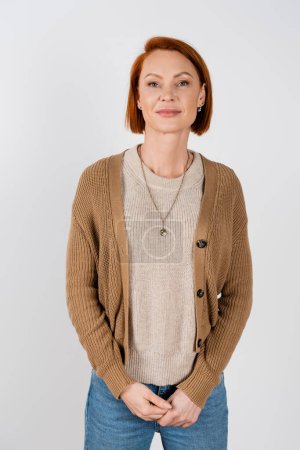 Smiling red haired woman in casual clothes looking at camera isolated on grey 