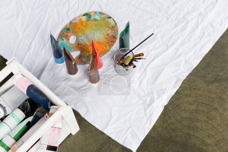 Top view of paints and palette on white cloth on floor 