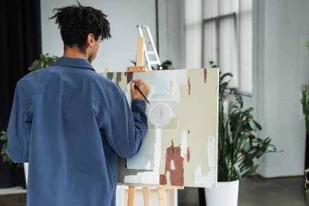 Back view of african american man painting on canvas in studio 