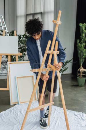 African american artist adjusting easel on cloth in studio 