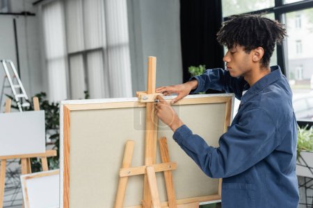 Photo for Side view of young african american artist adjusting easel with canvas in workshop - Royalty Free Image