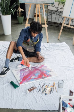 African american artist pouring paint on canvas on cloth in studio 