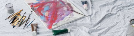 High angle view of paintbrushes near paints and drawing on cloth, banner 