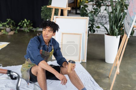 Jeune artiste afro-américain tenant une tasse en papier et un pinceau en atelier 