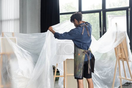 Artiste afro-américain couvrant chevalet et toile de polyéthylène en atelier  