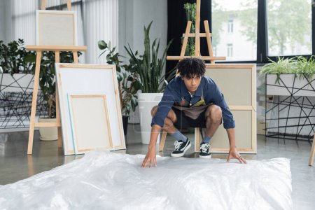 Young african american artist putting cellophane on floor in studio 