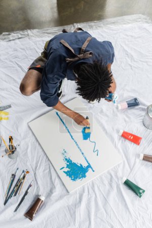 Overhead view of african american artist painting on canvas on floor in studio 