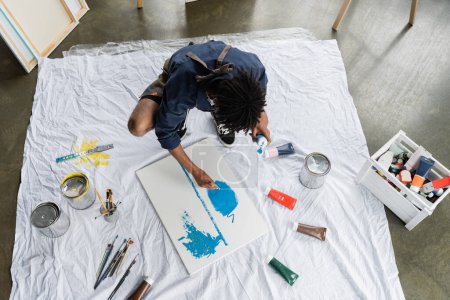 Téléchargez les photos : Overhead view of african american artist painting on canvas near paints on floor in studio - en image libre de droit