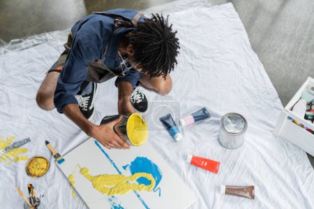Photo for Overhead view of african american artist pouring paint on canvas in studio - Royalty Free Image