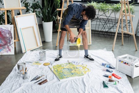 Joven artista afroamericano vertiendo pintura sobre lienzo y tela en taller de arte 