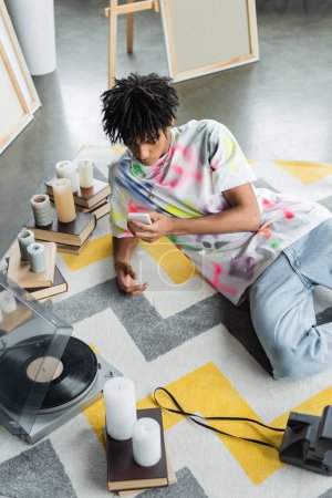 High angle view of african american artist using smartphone near record player and books in studio 