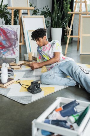 African american artist using cellphone near vintage camera and books in studio 