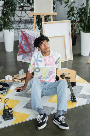 Junge afrikanisch-amerikanische Künstlerin sitzt neben Smartphone und Akustikgitarre im Studio 