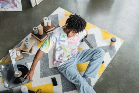Overhead view of african american artist using record player near books and smartphone in studio 