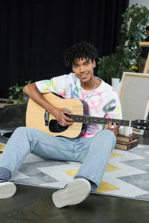 Smiling african american artist playing acoustic guitar in studio 