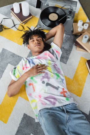 Téléchargez les photos : Vue du dessus de l'artiste afro-américain couché près du tourne-disque et des livres en atelier - en image libre de droit