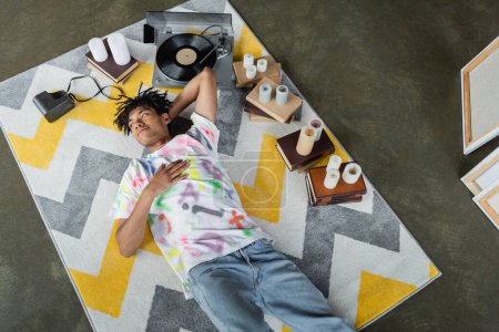 Top view of african american artist lying near vinyl layer and books in studio 